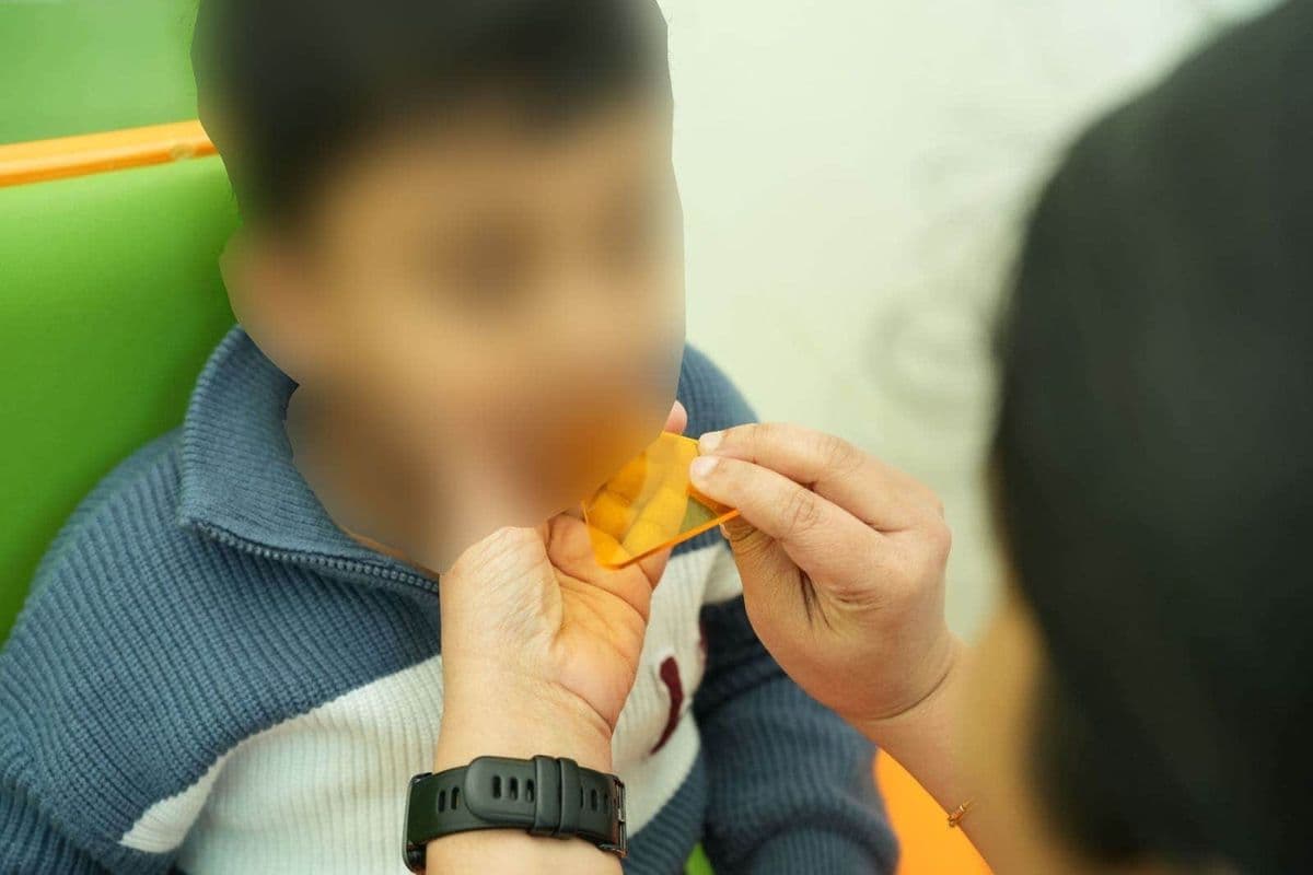 therapist holds a small orange plastic shape up to a child's mouth during an early intervention therapy activity.