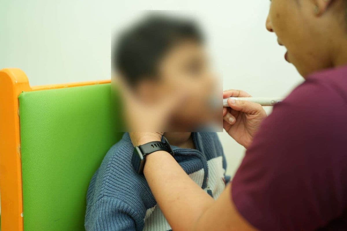A speech therapist uses a specialized oral motor tool to assist a young child during an active speech therapy session.