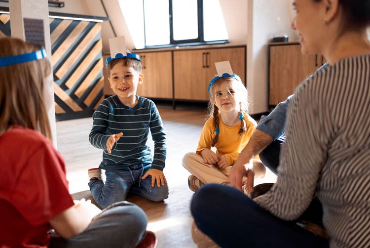 Children wearing headbands sitting in a circle on the floor during a fun group therapy or classroom game.