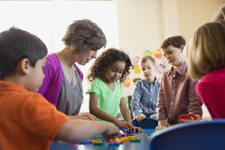 Early childhood educator guiding young children through a tabletop learning activity with colorful blocks.