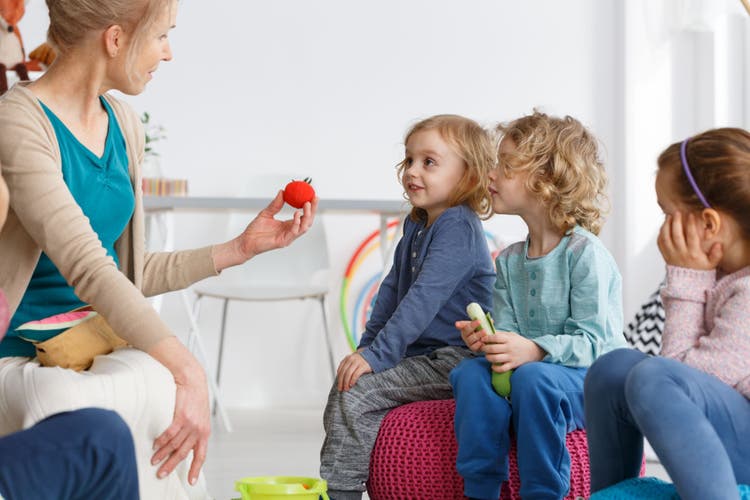 Female therapist showing a small toy to a group of children during an interactive group speech therapy session.